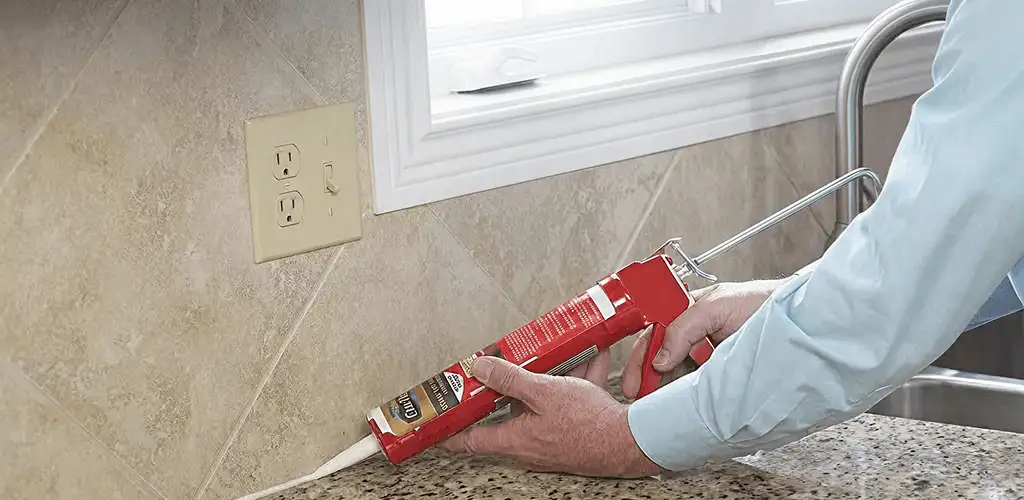Handyman applying caulk along a kitchen backsplash and countertop seam in Dallas, TX